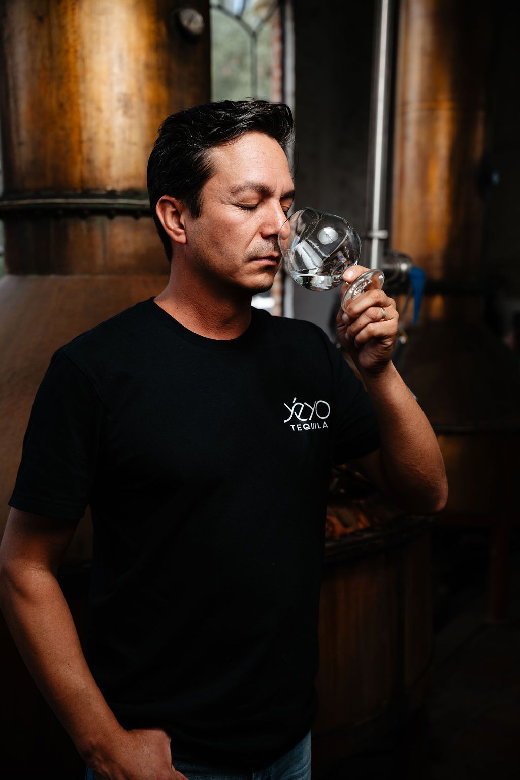 Cesar Vivanco smelling a tasting glass beside copper distilling vessels