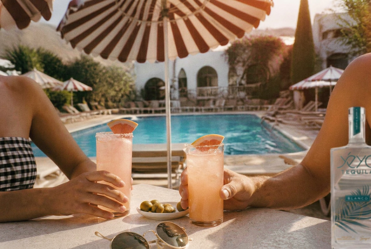 Two Palomas and a plate of olives beneath a striped umbrella